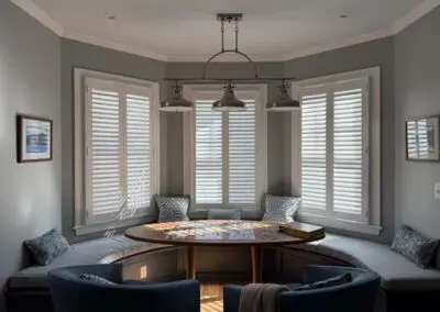Cozy breakfast nook with round table, built-in seating, gray shutters.