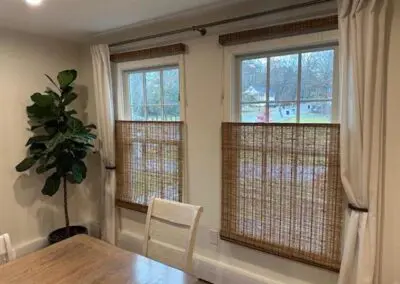 Dining room with bamboo blinds, wooden table, and potted plant.