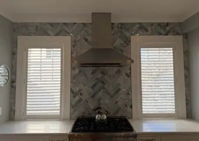 Modern kitchen backsplash with stainless steel range hood between two windows.