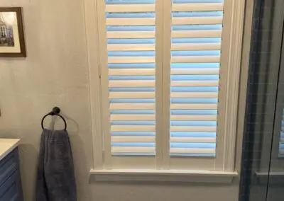 White plantation shutters in bathroom with blue towel and patterned floor tiles.