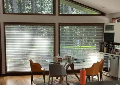 Modern dining area with large windows, stylish chairs, glass table.