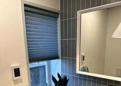 Blue bathroom window shades complementing modern tiled wall and mirror design.